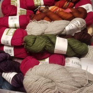 View of a container of stashed yarn, including red, green, purple, and grey skeins of different sizes.