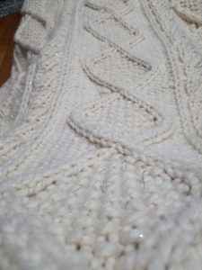 In progress cabled afghan, stretched over the writer's legs to show off the center diamond panel and bordering cables.