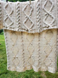 View of the finished afghan hanging on a clothesline to dry, showing both the front and reverse of the cables.